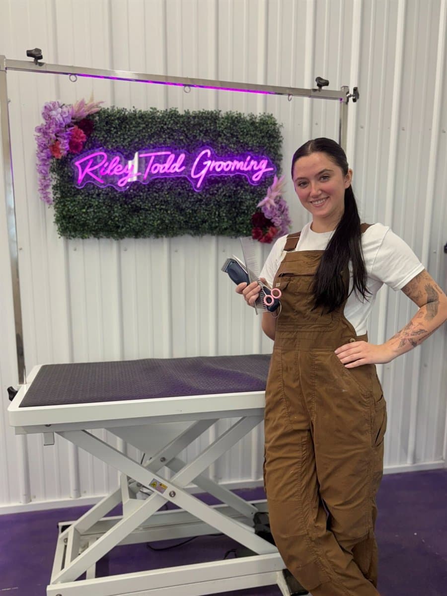 Riley Todd holding her clippers and shears in front of the Riley Todd Grooming sign